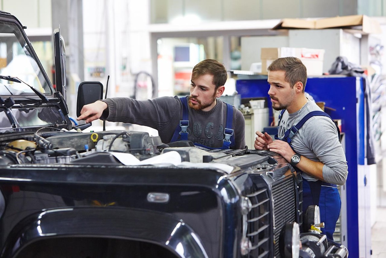 Zwei Männer arbeiten an einem Auto mit geöffneter Motorhaube
