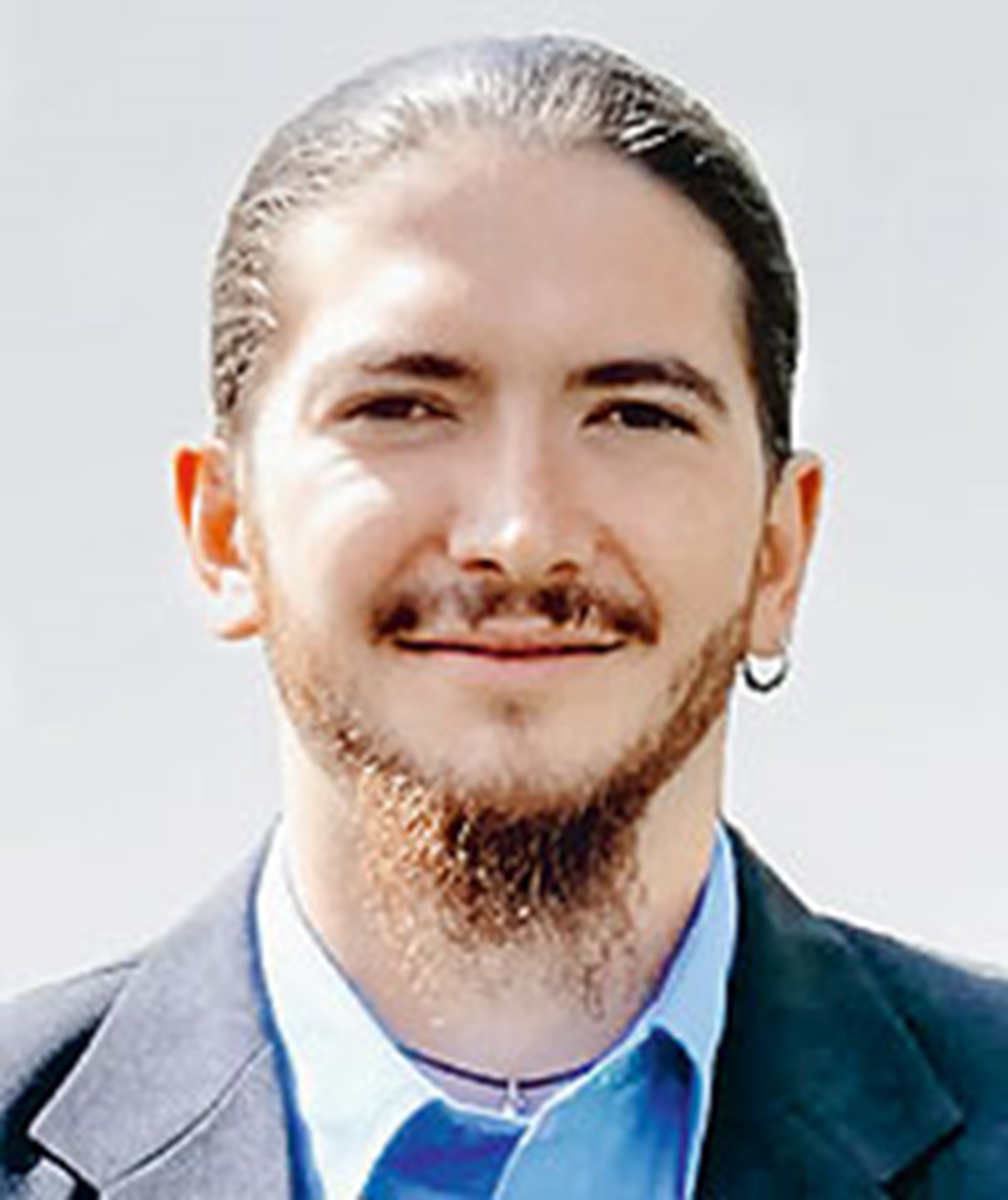 Ein Mann mit einem Bart trägt ein blaues Hemd und blickt in die Kamera.